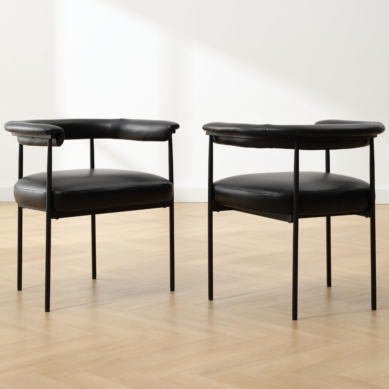 Two black faux-leather barrel dining chairs with curved arms and black legs
