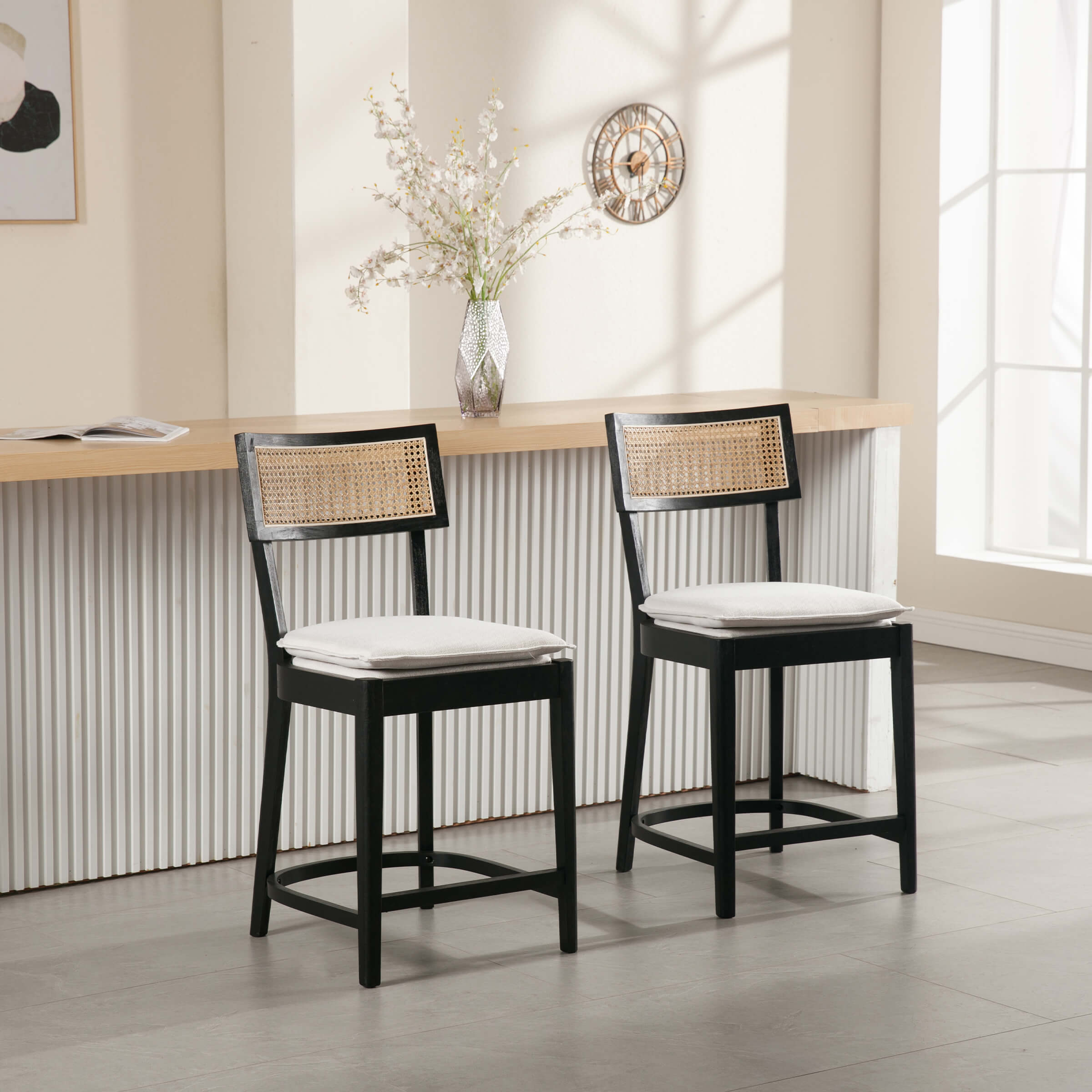 Two black wood counter stools with woven cane backrests and white seat cushions in a bar setting