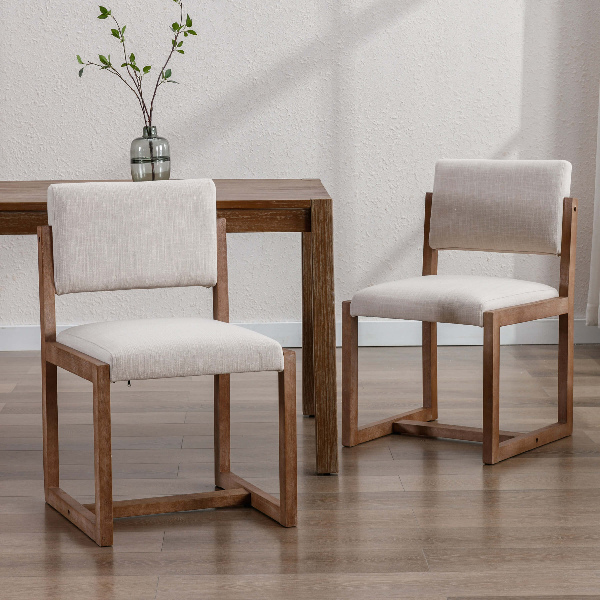 Two upholstered wood dining chairs with light beige fabric around a wooden table