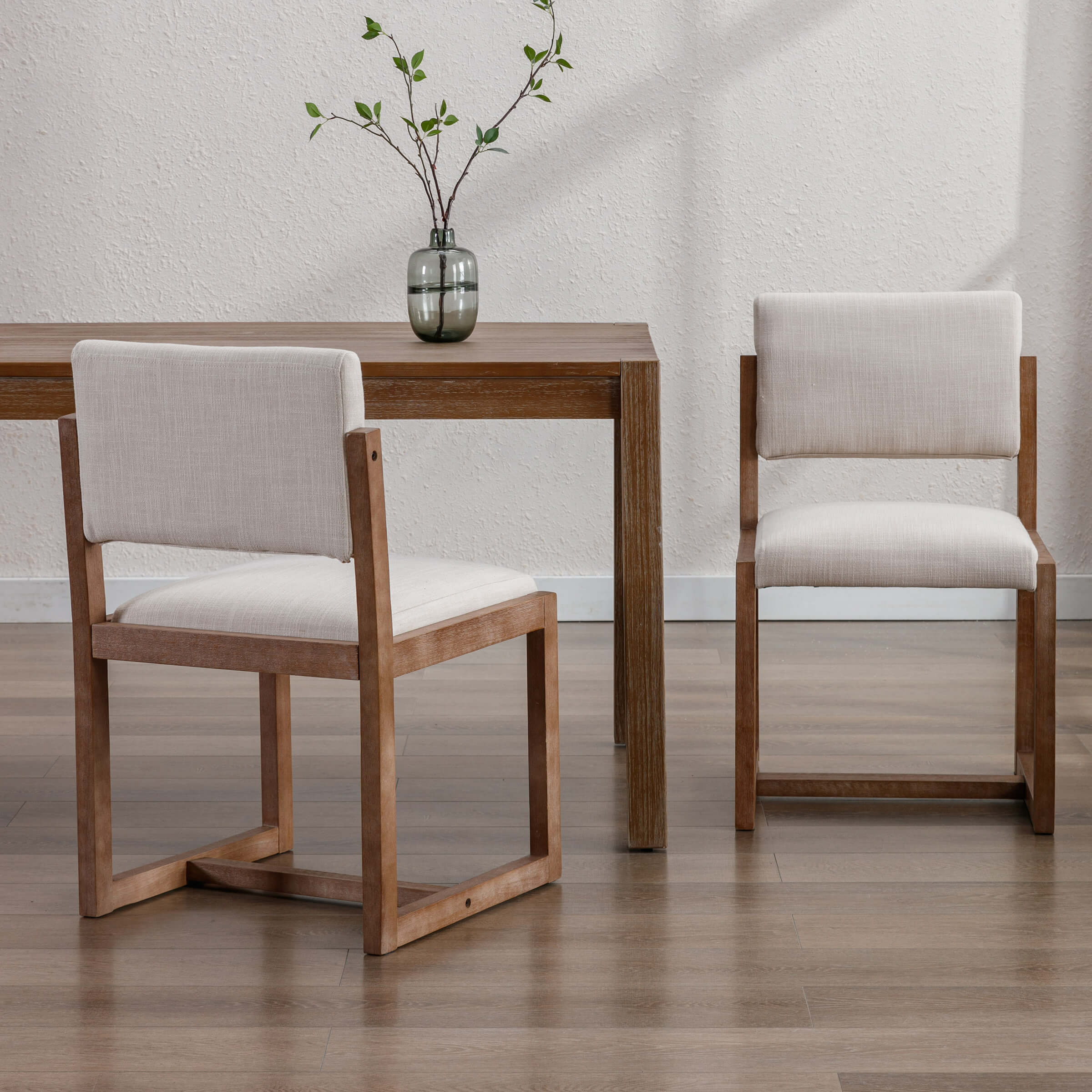 Two upholstered wood dining chairs with light beige fabric around a wooden table (different angle)