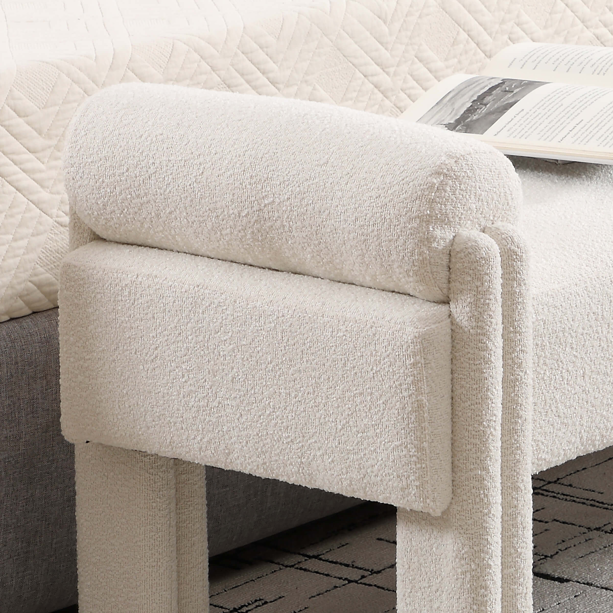 Close-up of end of bed bench with textured beige upholstery showing armrest and cushion