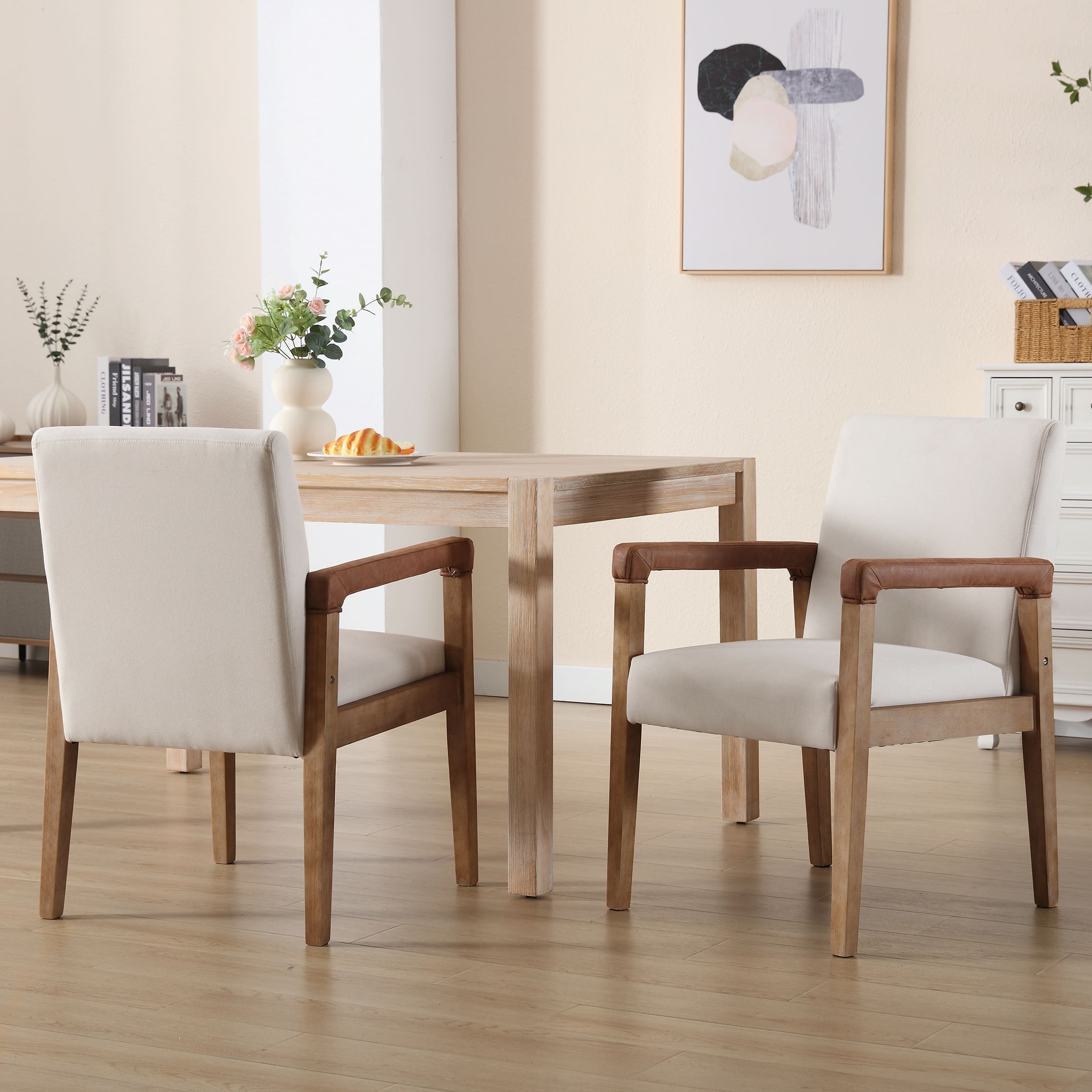 Two mid-century wooden dining chairs with brown leather arms around a wooden table in a bright room