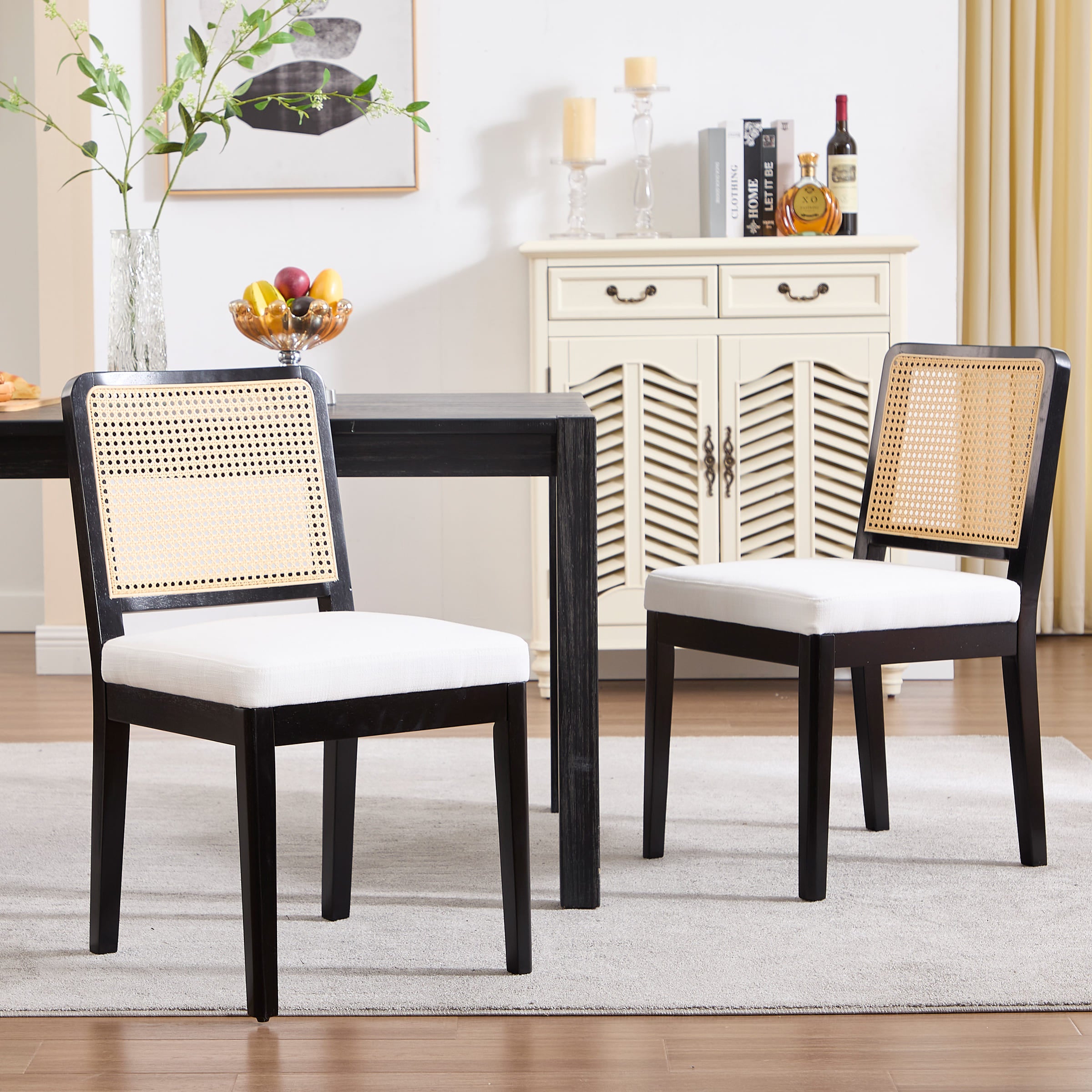Two black dining chairs with woven cane backrests and white seat cushions around a dark wood table