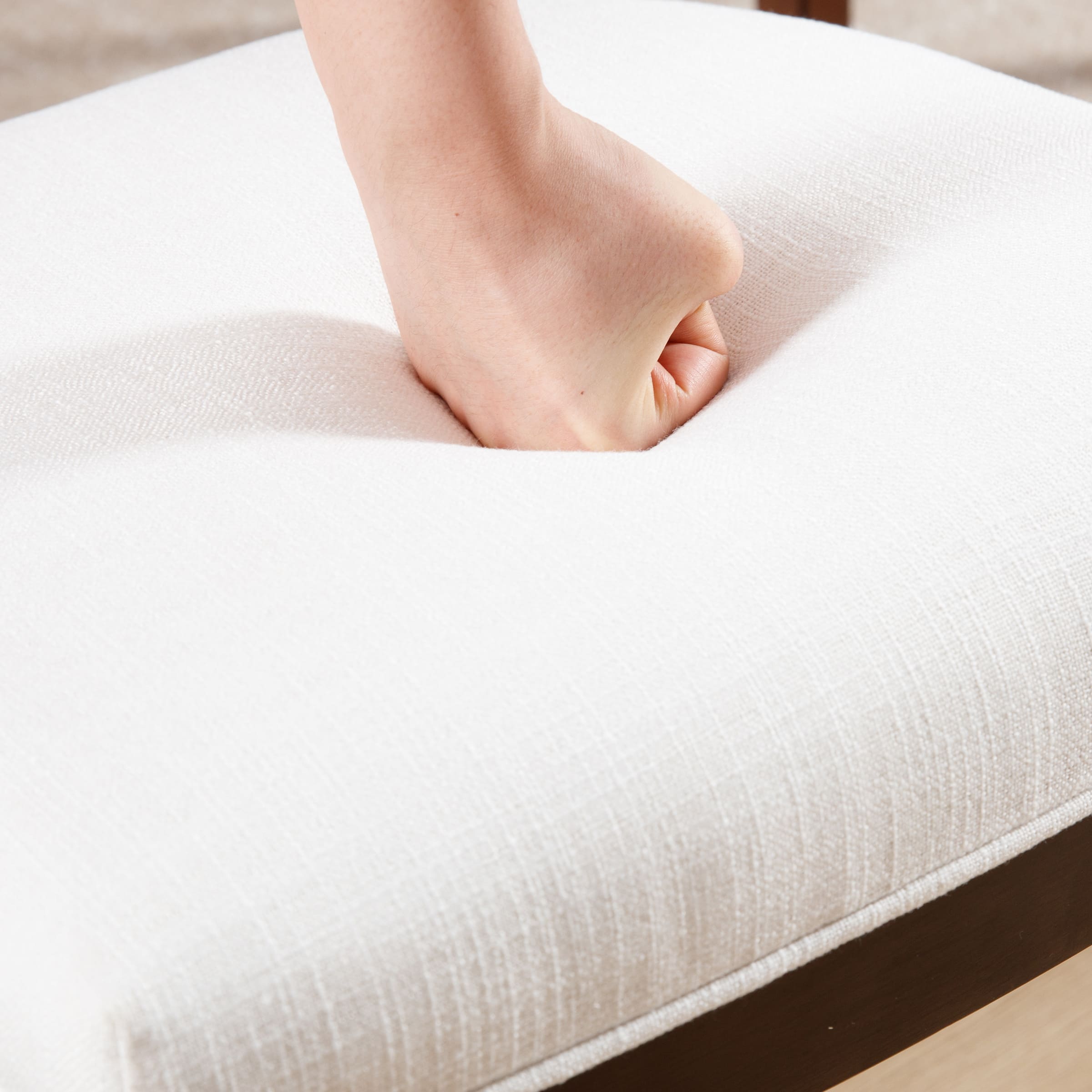 Close-up of white upholstered seat cushion being pressed