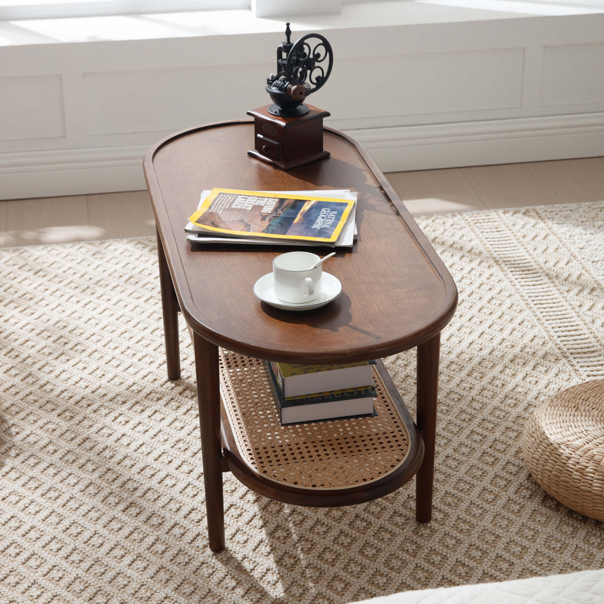 Oval coffee table with cups and magazines on top and a lower shelf with books in a bright room