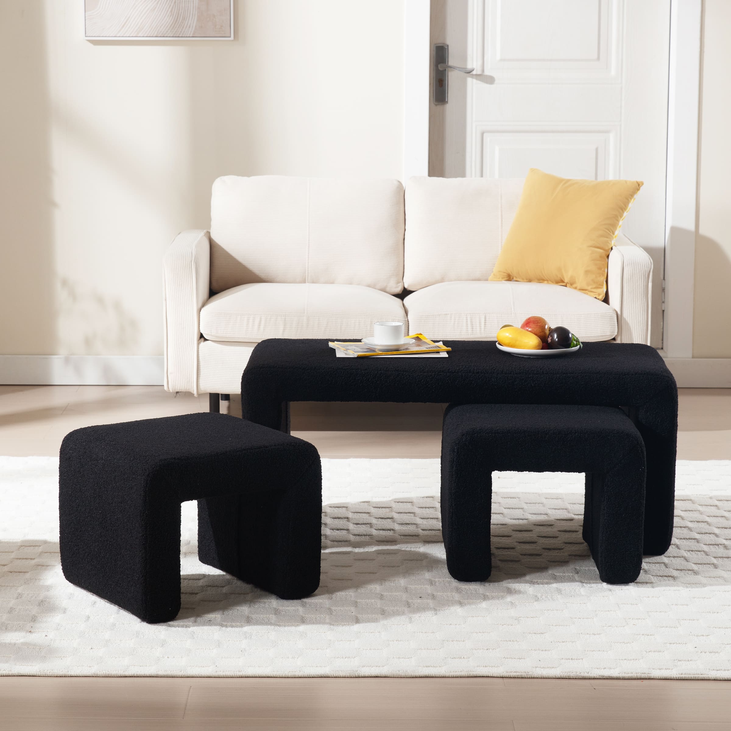 Set of three black boucle ottomans with curved edges placed in living room