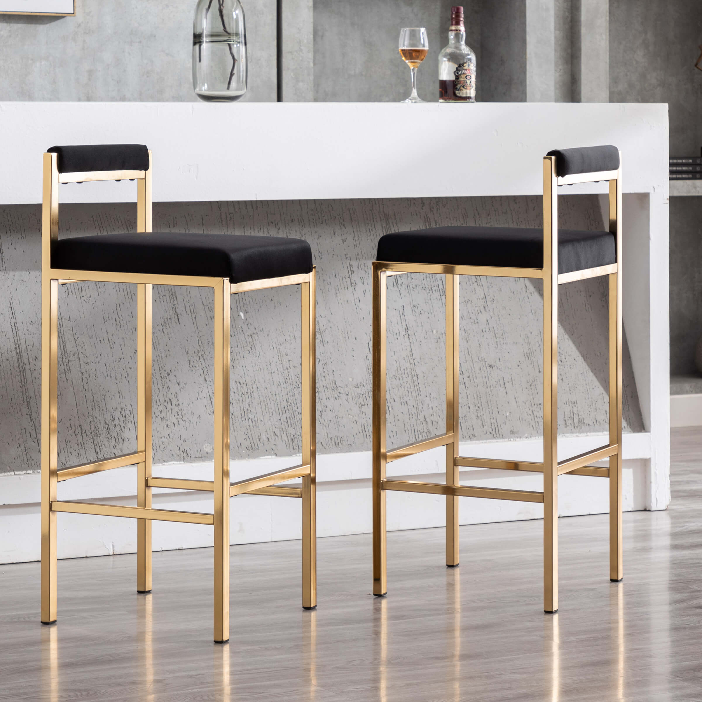 Two gold bar stools with black cushions shown from a side angle